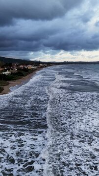 Vertical Aerial Drone Shot of Acharavi Beach North Corfu Greece Showing Stormy Sea Waves Crashing on Sandy Shore Under Dark Clouds Perfect for Social Media Stories Reels and Backgrounds