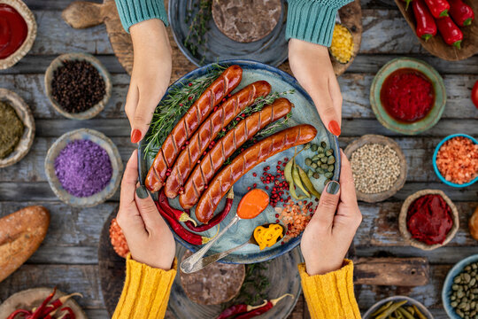 Grilled bratwurst and sausages in the plate at the hands of two women.  
