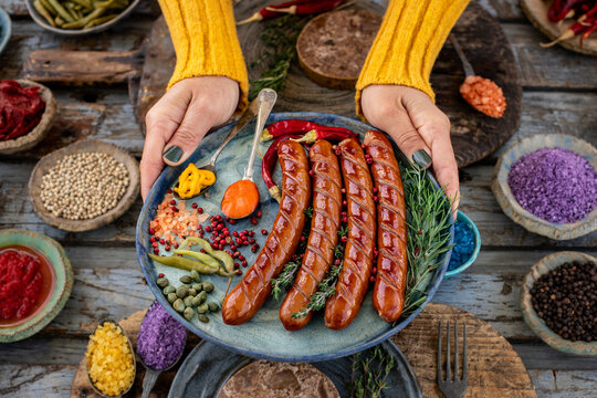 Grilled bratwurst and sausages in the plate at the hands of two women.  
