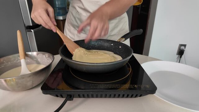 The hands of a woman who fries pancakes. A woman flips pancakes with a wooden spatula.