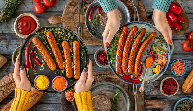 Grilled bratwurst and sausages in the plate at the hands of two women.  
