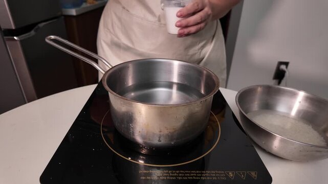 Woman turns on the induction hob and pours salt into a pot of boiling water