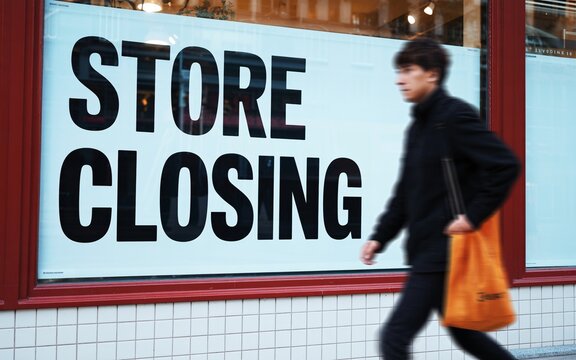 Store closing sale sign with person walking by in front of retail store window