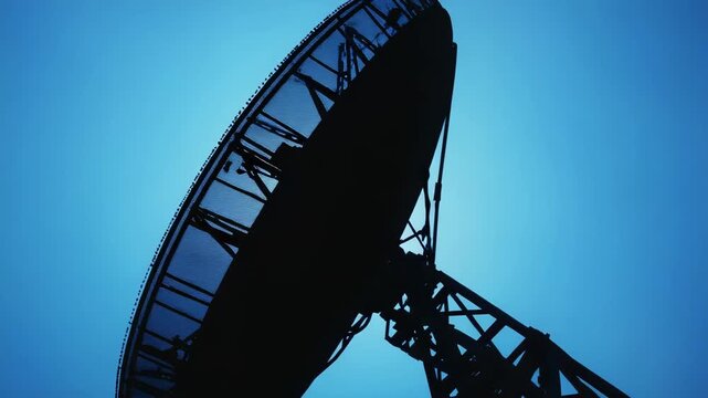 Large radio telescope silhouetted against a bright blue sky, collecting data and transmitting signals for scientific research and astronomical discovery