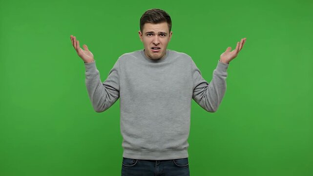 Confused Young Man With Hands Out In Questioning Gesture Against A Green Screen Background Wearing A Grey Sweatshirt And Blue Jeans With A