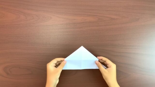 Two hands are folding a white piece of paper on a wood table