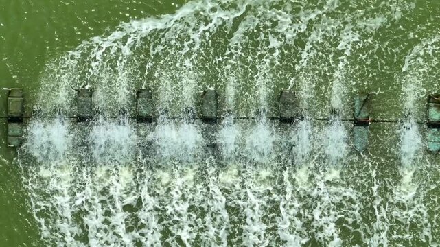 Aerial shot of paddle wheel aerators churning water in a farming pond, representing oxygenation systems, aquaculture innovation, water management, and enhanced aquatic growth conditions. Thailand.
