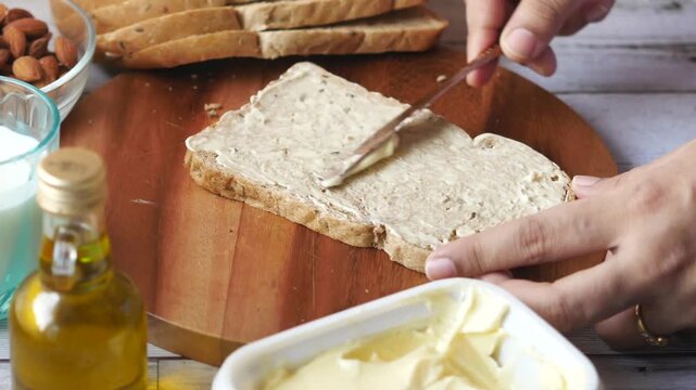 Close up view of hand spreading butter on brown bread slice with knife for breakfast preparation on wooden board