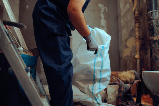 Construction Worker Handles a Heavy-duty Debris Bag. Laborer holding a rugged waste sack at the working site 
