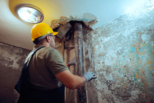 Plumber Inspecting a Pipe and the Ceiling of a Bathroom in renovation. Plumbing expert assesses the overhead structure and piping in a washroom 
