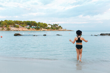 Obraz premium rear view of a girl in the swimsuit entering the water on the beach