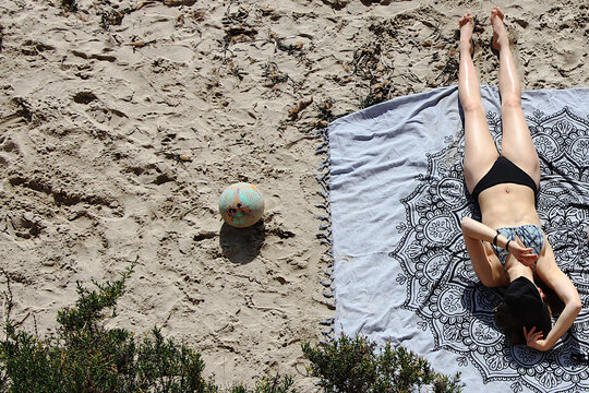 Mujer tumbada tomando el sol en la playa en verano con toalla, gorra y bal&oacute;n en vacaciones 