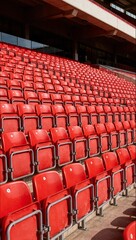 Obraz premium Rows of empty red plastic seats fill the grandstand of a modern sports stadium, waiting for fans to arrive for the game.