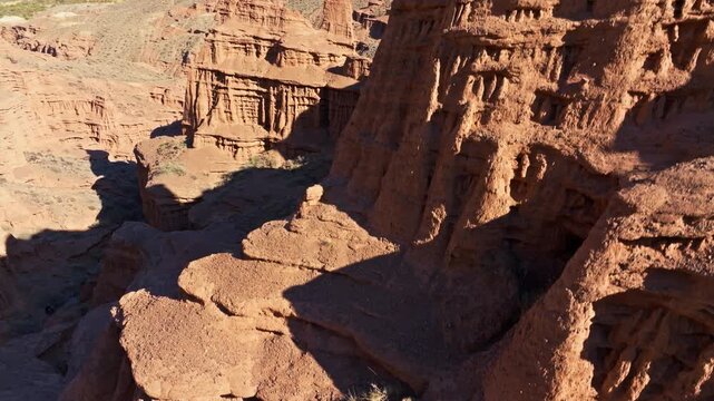 Dramatic red castle rock formations in arid canyon landscape, ascending drone view.