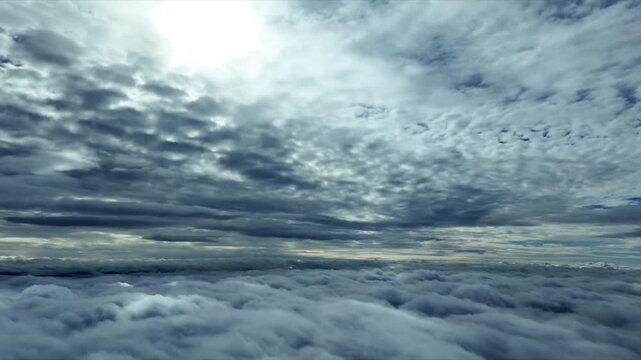 Hyperlapse x4 speed of a peacefull flight between layers of ethereal clouds with a shining sun above in a blue sky. Aerial footage taken from a jet cockpit.