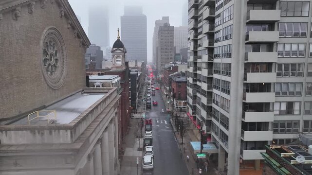 Downtown American street on foggy winter day. Traffic lines narrow corridor between historic brick buildings and modern high-rise apartments fading into gray urban haze. Philadelphia, PA. Aerial view.