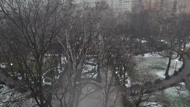 Rittenhouse Square in Philadelphia during winter. Bare trees and snow-dusted paths fade into fog as downtown buildings emerge through soft, misty skyline. Aerial rising Wide shot.