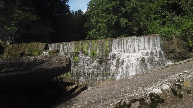 Beautiful waterfall flows over stepped rocks covered in green moss in a natural forest environment in Rupit, Catalonia, Spain, creating a serene and captivating landscape on a sunny day