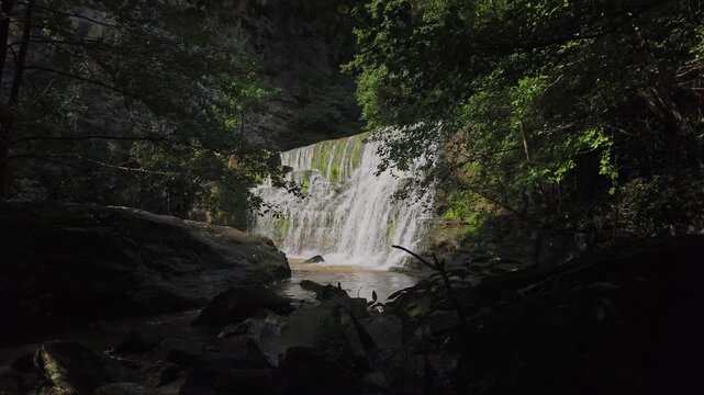Scenic view of a beautiful waterfall flowing vigorously over mossy rocks in a lush green forest, creating a small river in the peaceful wilderness of Rupit, Catalonia, Spain