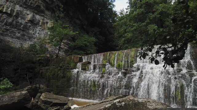 Crystal clear water flowing down over moss-covered rocks at the beautiful Sallent de Rupit waterfall, a majestic natural landmark hidden in the lush green forest of Catalonia, Spain
