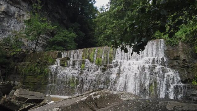 Majestic Salt de Sallent waterfall flowing down mossy, stepped rock formations in a lush green Catalan forest near the village of Rupit, creating a serene and powerful natural scene