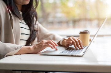 Close up of woman's hands typing on keyboard working on a laptop aside coffee while sitting at table