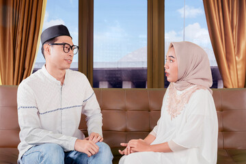 Obraz premium Young Asian Muslim Couple Sitting on Sofa Having Serious Conversation at Home
