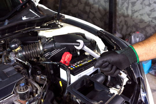 Professional Engine Maintenance, A mechanic's gloved hand holds a silver wrench over a vehicle's open engine bay, focusing on battery and component care.