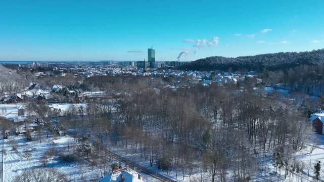 Stunning aerial shot of Gdansk in winter featuring snowcovered trees, residential houses, and the Olivia Star skyscraper under a clear blue sky.