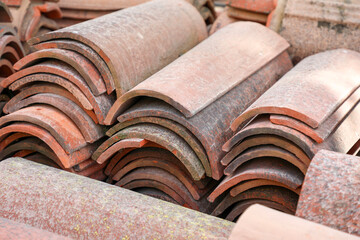 Weathered terracotta roof tiles with moss, stacked in neat piles, showing curved texture and aged patina for traditional roofing, renovation and architectural details