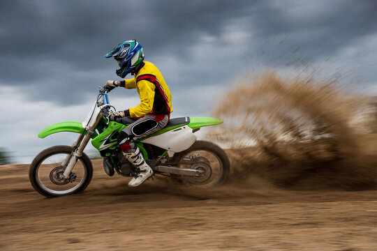 Solo motocross rider carving through a dirt berm on a track. Itense action with dust and sand roost. Moody extreme sports photography.  Grainy textured film look.