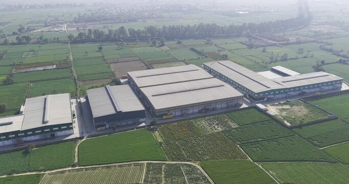 Drone view shows a large industrial factory or warehouse complex situated amidst agricultural fields