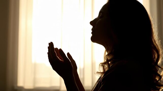  Her hands are raised with open palms facing upward. She is deeply backlit by bright, diffused morning sunlight streaming through sheer window curtains. 
