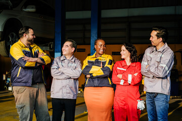 Auto repair team stands with arms crossed in a garage, smiling in work uniforms near a vehicle lift. © artitwpd
