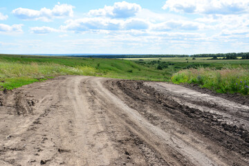 Muddy Dirt Road Winding with tracks Through a Green Hilly Landscape Under a Blue Sky copy space