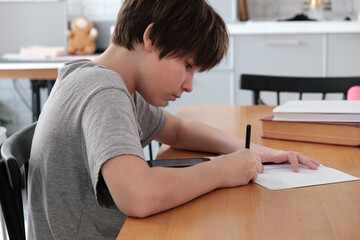 Obraz premium A teenager does his math homework, writes down examples in a notebook, and uses his smartphone for educational purposes. copying ready-made homework solutions. traditional and digital learning.
