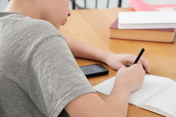 A teenager does his math homework, writes down examples in a notebook, and uses his smartphone for...