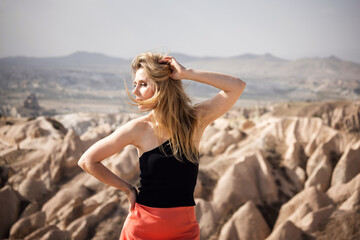 Woman in black top and red skirt posing on rocky mountain outdoors. Summer exploration, fashion, leisure, scenic view