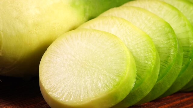 Fresh juicy slices of green radish moving slowly in studio light, macro texture.