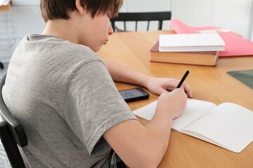 Obraz premium A teenager does his math homework, and uses his smartphone for educational purposes. copying ready-made homework solutions. a combination of traditional and digital learning.