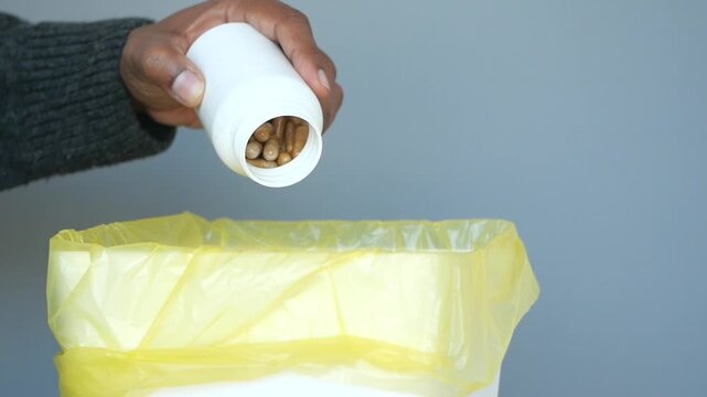 Close up of person discarding expired medication, pouring brown capsules into yellow garbage bag, promoting safe disposal of pharmaceuticals and preventing misuse or environmental contamination