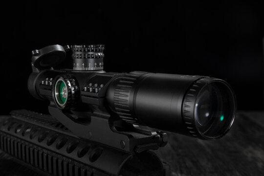 Close up of a tactical rifle scope mounted on a rail system against black background