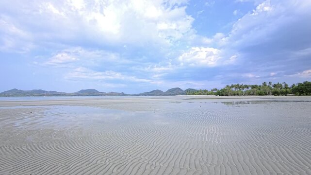 Rippled tidal sandflat facing distant palms under cloudy daylight in Thailand