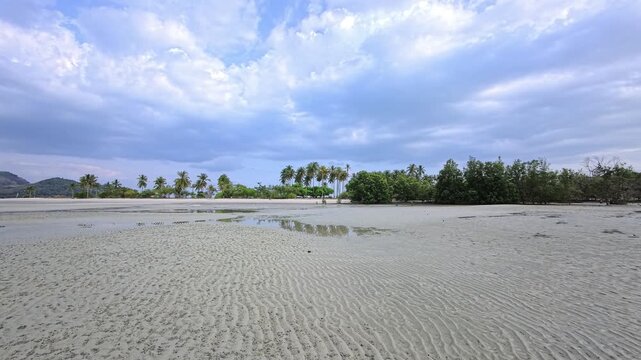 Shallow reflective pool across rippled tidal sandflat in Thailand