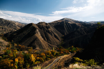 Mountain valley landscape with autumn forest and dramatic hills under blue sky