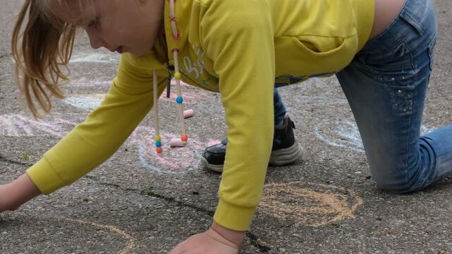 Child paints outdoors. Little girl drawing colored chalk on the asphalt . Creative development of children