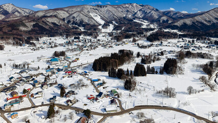 Fototapeta premium Sunny winter day overlooking a snowy rural valley and mountains with blue sky