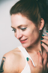 Naklejka premium Natürliches Frauenportrait mit sanftem Lächeln und grün lackierten Nägeln. Warmes Licht, Tattoo-Detail und zarte Pose – modernes Beauty- und Lifestyle-Foto mit authentischer Ausstrahlung.