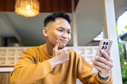 Confused Asian man thinking while looking at his smartphone