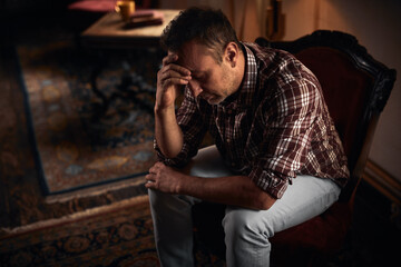 Obraz premium Man with headache, depression, sadness and loneliness sitting on a chair at home.